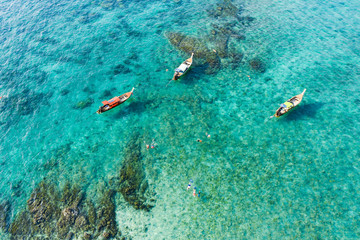 View from above, stunning aerial view of some long-tails boats and tourists who do snorkeling in a beautiful, transparent and turquoise sea, Phi Phi Island, Thailand.