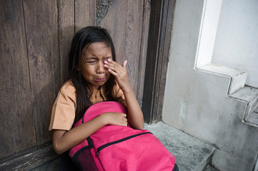 7 or 8 years child in school uniform sitting outdoors on the floor crying sad and depressed holding...