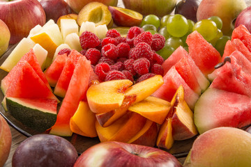 A mixture of their fruit. Peach, grapes, apple, watermelon, melon, raspberry, plum. Juicy and ripe pieces of fruit close-up.