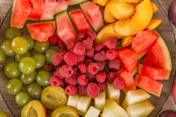 A mixture of their fruit. Peach, grapes, apple, watermelon, melon, raspberry, plum. Juicy and ripe pieces of fruit close-up. View from the top, Flat Lay.