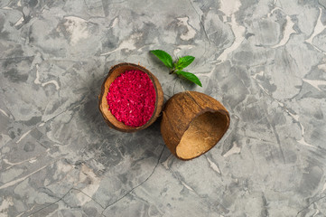 Half of coconut with red coconut flakes and leaves of fresh mint on old gray concrete. Top view