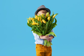 Cute smiling child holding a beautiful bouquet of yellow tulips in front of his face isolated on...