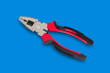 One new metal pliers with rubber handles black and red color in center on blue table. Top view. Repair or building concept