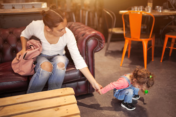 Mom and daughter are sitting in a restaurant awaiting their order. A small child is played on the...