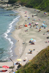 A small wild beach in the summer. Tourists relax on the sunny day. Umbrellas and swimwear in the sand. Picture from above.