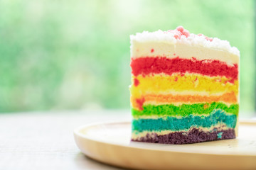 Rainbow cake placed on a wooden plate with nature green bokeh background with natural light.