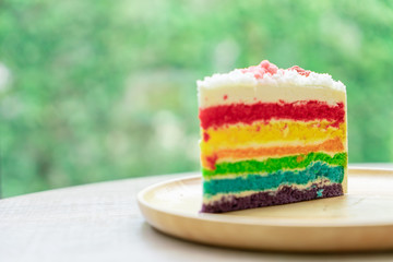 Rainbow cake placed on a wooden plate with nature green bokeh background with natural light.