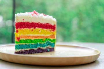 Rainbow cake placed on a wooden plate with nature green bokeh background with natural light.