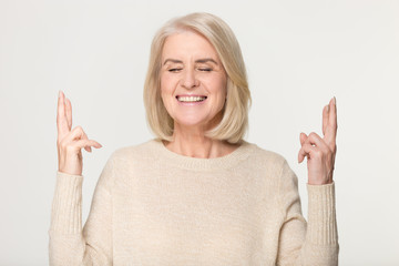 Happy middle aged woman crossing fingers hoping for good luck