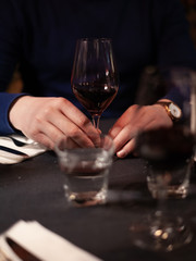 hands of a man sitting at a table in a restaurant, in front of him is a glass of wine