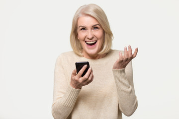 Excited mature woman holding phone amazed by mobile win