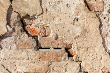 Old cracked and ruined wall made of red bricks with remains of plaster. Grunge Background Stucco on a old brick wall.