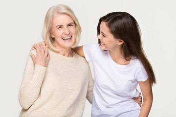 Cheerful young daughter embracing old mom isolated on background