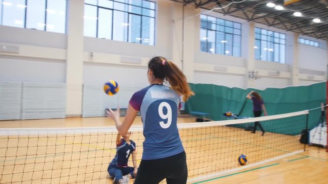 Sports for disabled people. A young woman sitting on the floor and playing volleyball with her trainer standing up