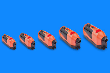 Horizontal row of many red and black plastic laser levels with water bubble for horizontal or vertical measure from small to large on blue background