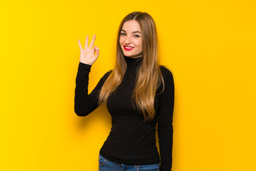 Young pretty woman over yellow background showing an ok sign with fingers