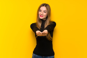 Young pretty woman over yellow background holding copyspace imaginary on the palm to insert an ad