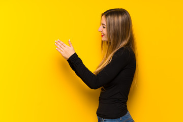 Young pretty woman over yellow background applauding after presentation in a conference