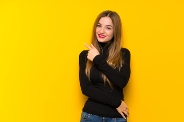 Young pretty woman over yellow background pointing to the side to present a product