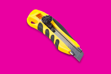 One stationery knife with yellow and black plastic handle in center of pink background