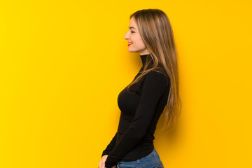 Young pretty woman over yellow background in lateral position