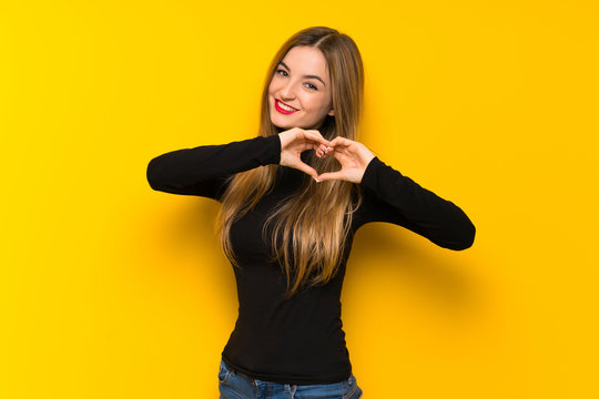 Young Pretty Woman Over Yellow Background Making Heart Symbol By Hands