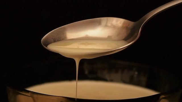 Iron spoon with condensed milk on a dark background