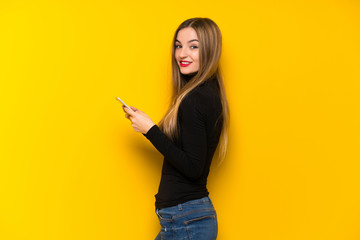 Young pretty woman over yellow background sending a message with the mobile