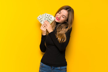 Young pretty woman over yellow background taking a lot of money
