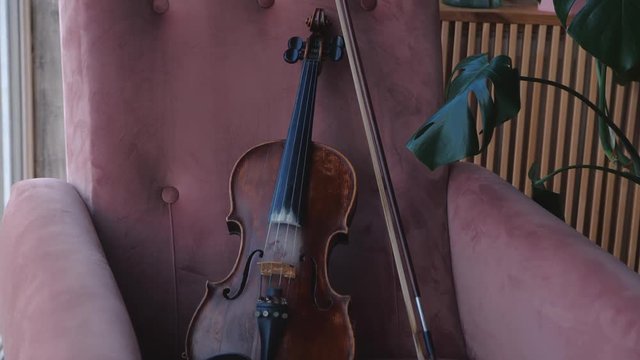 Violin with bow lying chair in room near window. Steady cam shot.