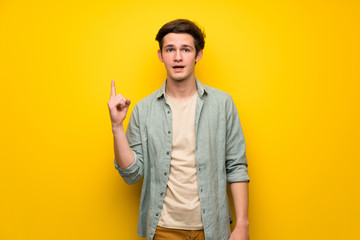 Teenager man over yellow wall thinking an idea pointing the finger up