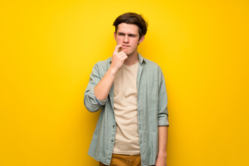 Teenager man over yellow wall having doubts while looking up