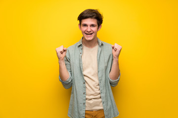 Teenager man over yellow wall celebrating a victory in winner position