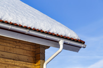 Wood log house with white rain gutter and down pipe and tiling roof covered with snow on blue sky...