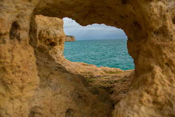 The hole is a cave in the yellow rock, through which you can see the blue water of the Atlantic Ocean and the precipice of the opposite shore in the Algarve, Portugal.
