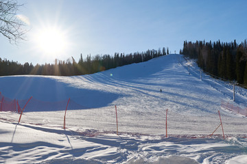 Skiers and snowboarders riding on a ski slope in mountain resort on winter day at sunset time