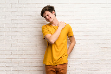 Teenager man over white brick wall suffering from pain in shoulder for having made an effort