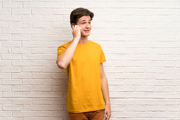 Teenager man over white brick wall keeping a conversation with the mobile phone