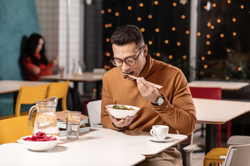 Customer sitting in restaurant and learning to eat a dish with Chinese chopsticks.