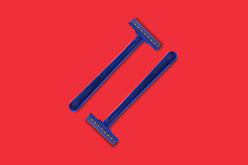 Pair of male disposable plastic razors blue color with two sharp blades in center on red table in bathroom. Top view. Hygiene concept