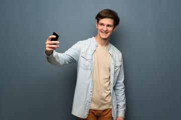 Teenager man with jean jacket over grey wall making a selfie