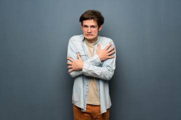 Teenager man with jean jacket over grey wall freezing