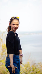 Women white skin lovely brown hair a small woman red lips wearing a black shirt wearing a blue gene woman Wearing yellow glasses stand  poses photography portrait which has water in back in the park.
