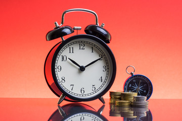 Alarm Clock, compass and coins on red background with selective focus and crop fragment. Copy space  and business concept