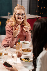 Young woman sitting at the table in cafe and asking her friend about telephone.