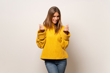 Woman with yellow sweater over isolated wall making money gesture