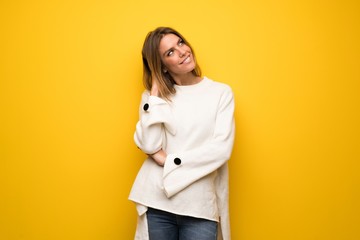 Blonde woman over yellow wall thinking an idea while scratching head