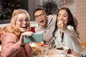 Two girls and boy taking selfie at the table after eating.