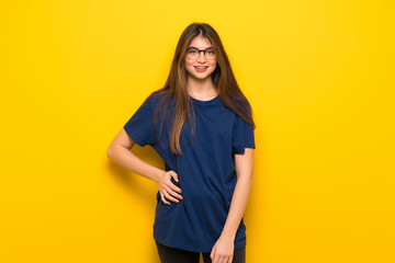 Young woman with glasses over yellow wall posing and laughing looking to the front