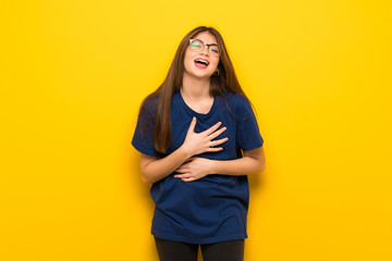 Young woman with glasses over yellow wall smiling a lot while putting hands on chest